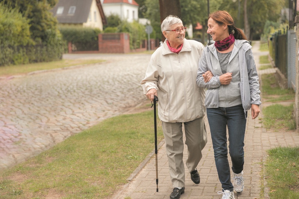 Happy senior woman and caregiver walking outdoors