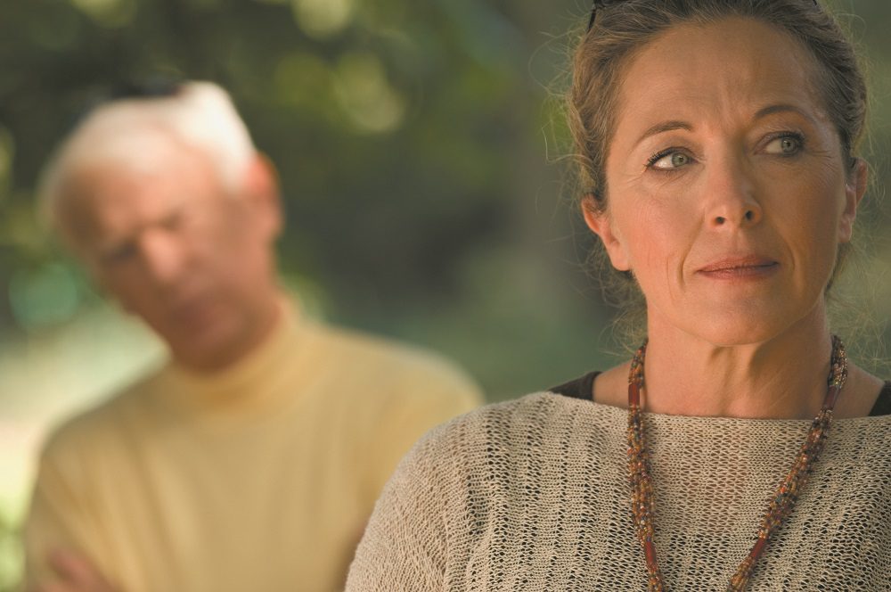 A sad woman, man blurred in the background.