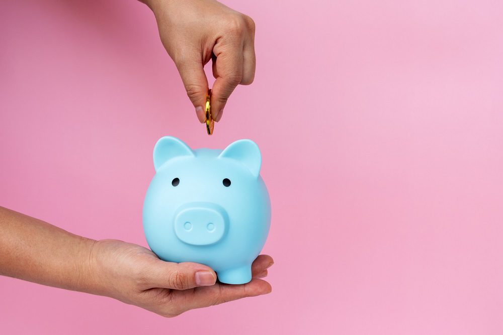 Woman Hand Inserting Coin into Piggy Bank