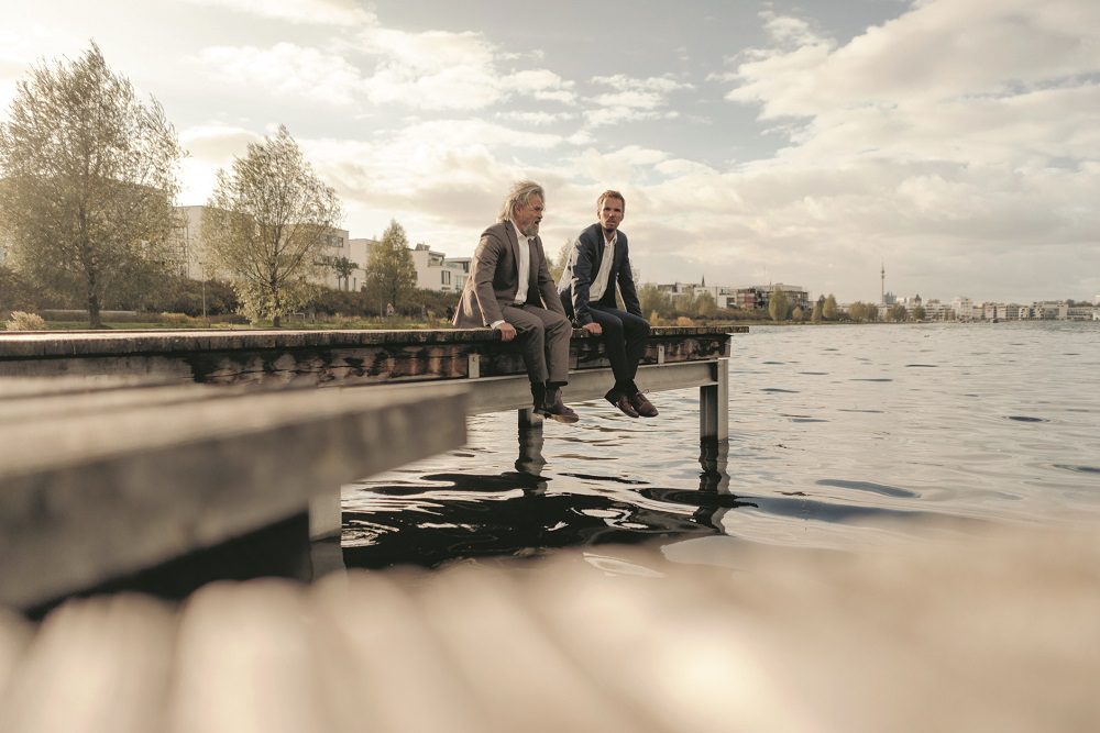 Two businessmen sitting on jetty at a lake