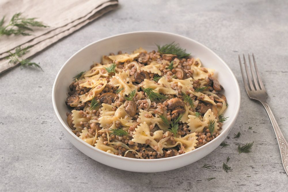 Traditional Jewish dish kasha varnishkes: buckwheat, pasta, champignon mushrooms, fried onions with herbs on a gray textured background, vegan food