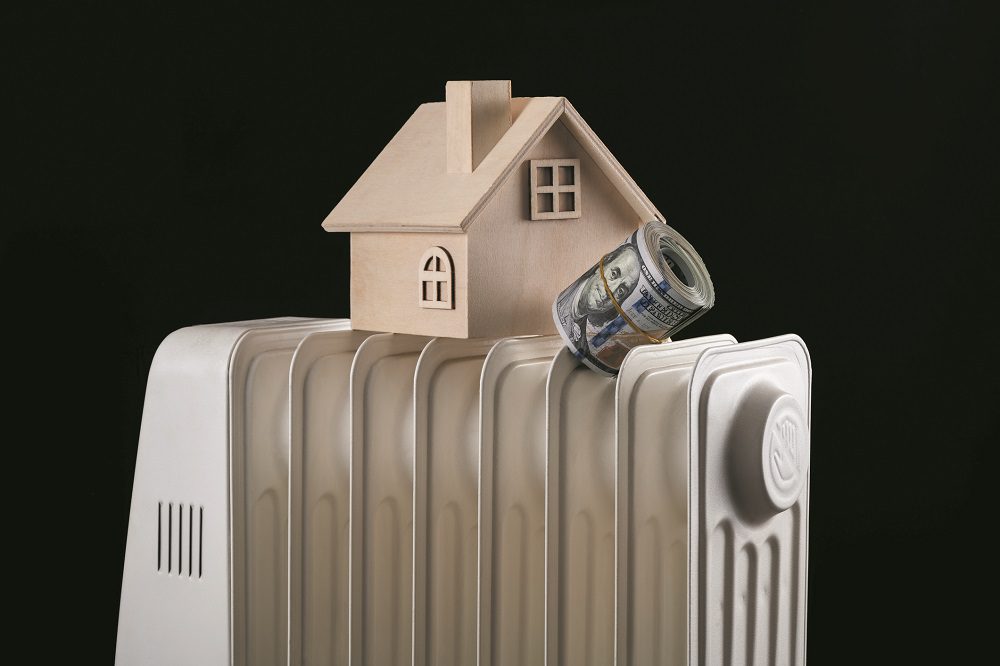 A stack of 100 American dollars banknotes, a symbolic wooden house and an electric heating battery on a black background