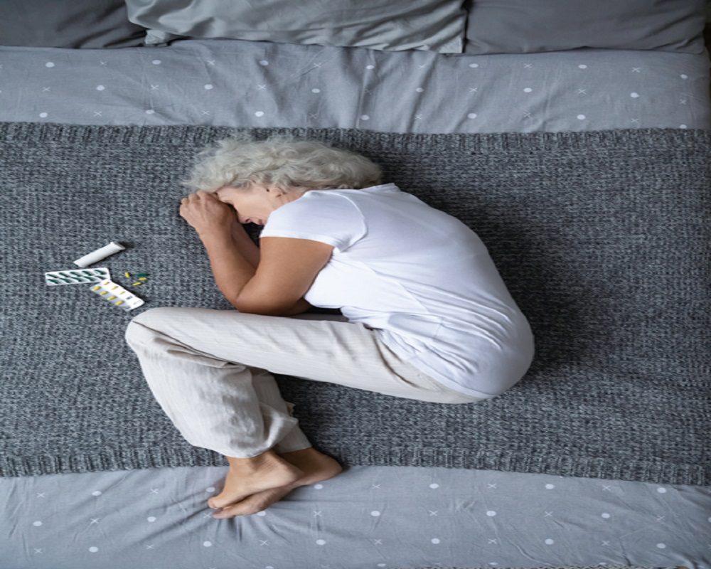Stressed mature retired woman lying on bed in fetal position.