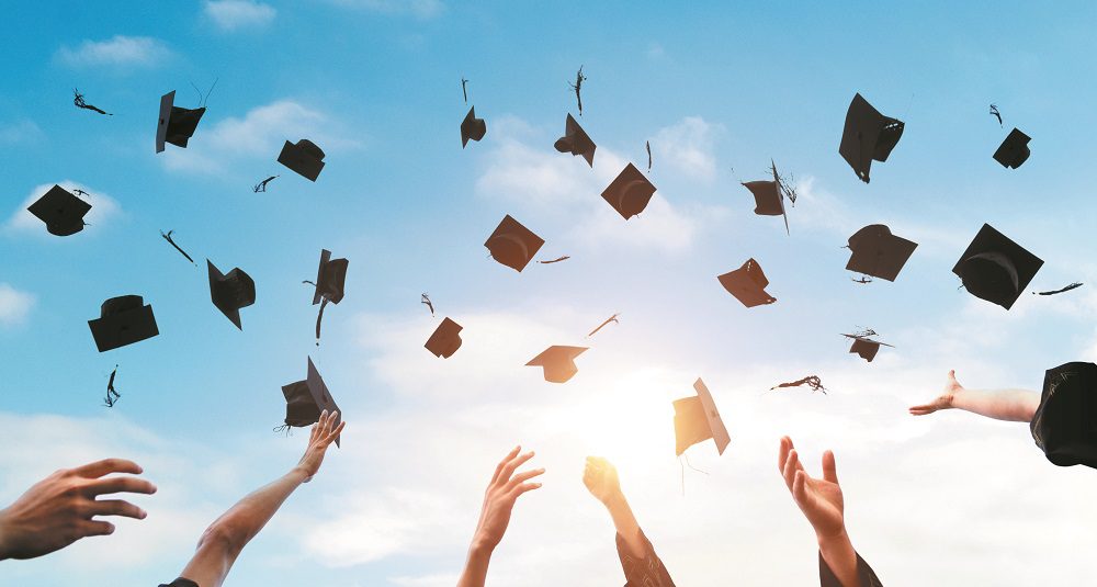 Graduating students hands throwing graduation caps in the air