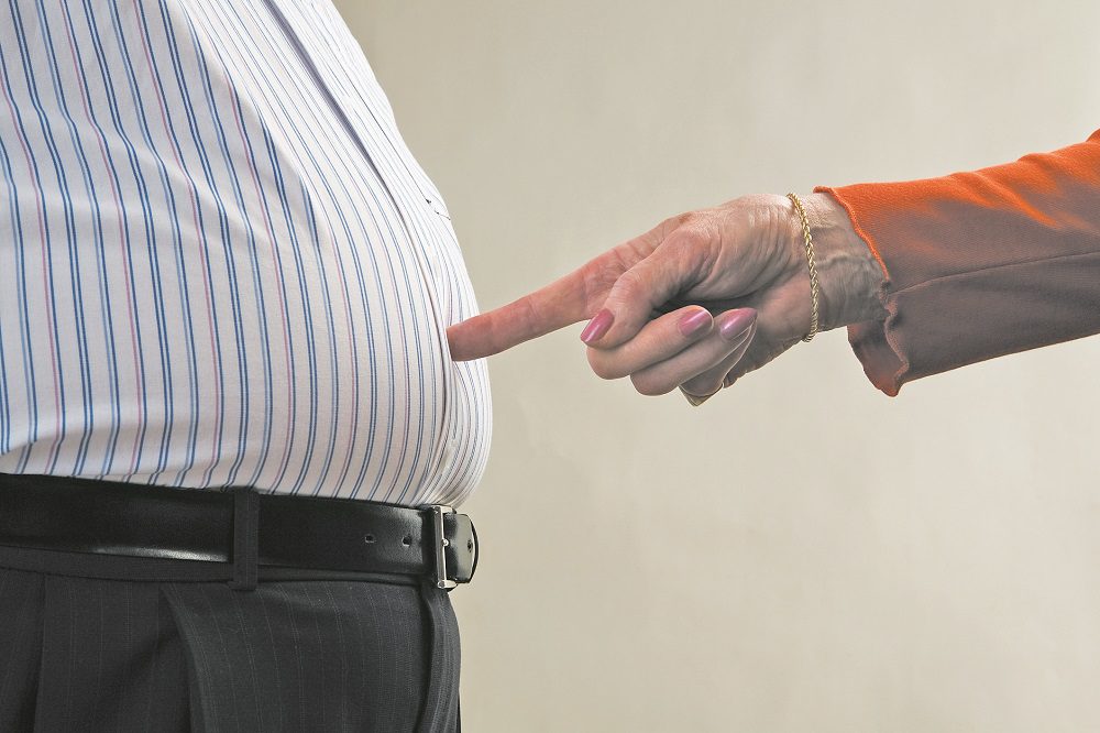 Woman pointing at senior man's stomach, close-up