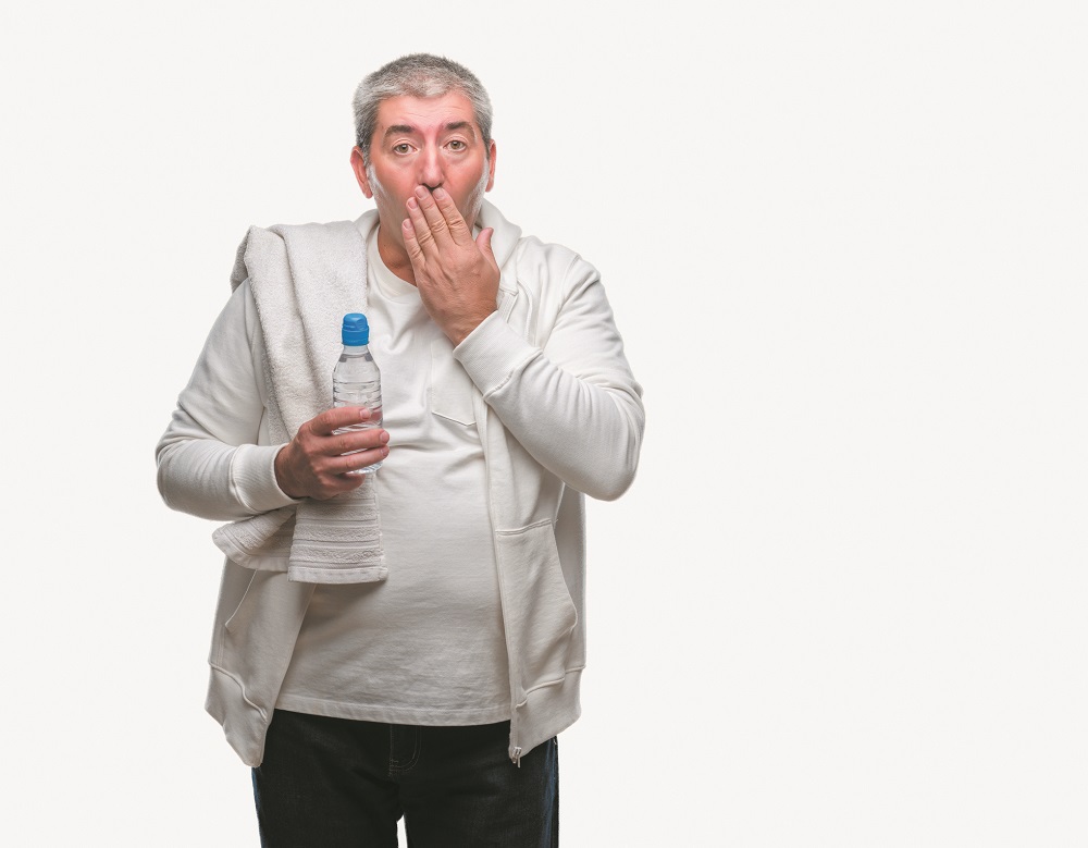 Handsome senior man training holding towel and water bottle over isolated background cover mouth with hand shocked with shame for mistake, expression of fear, scared in silence, secret concept