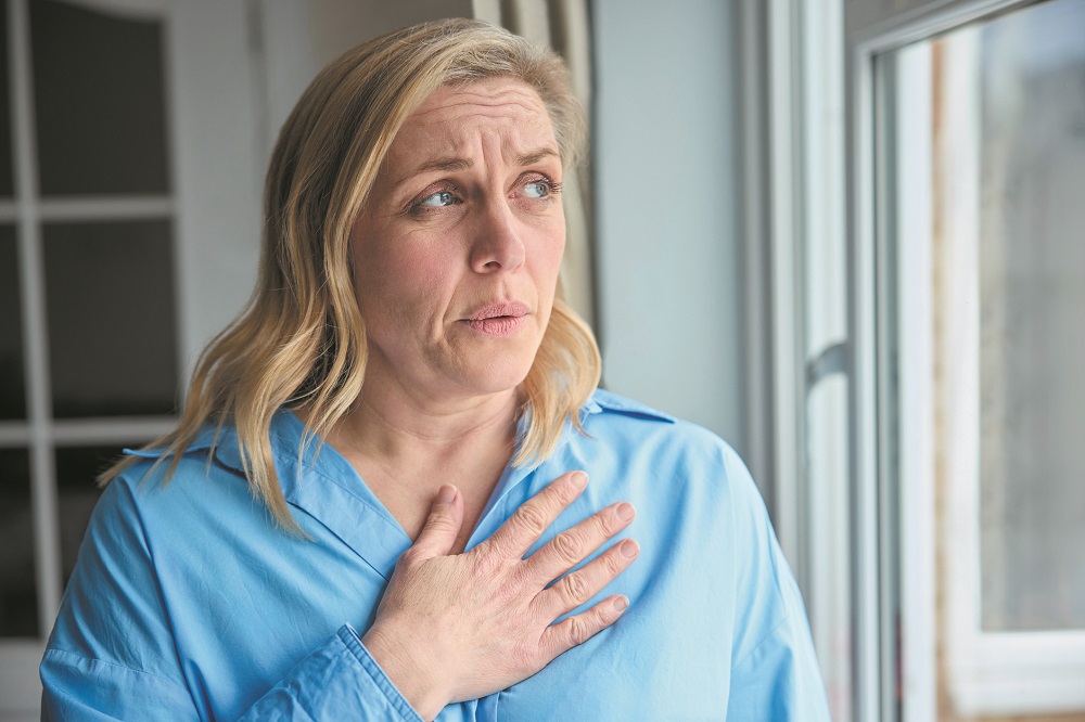 Menopausal Mature Woman At Home Standing By Window Suffering With Heart Palpitations