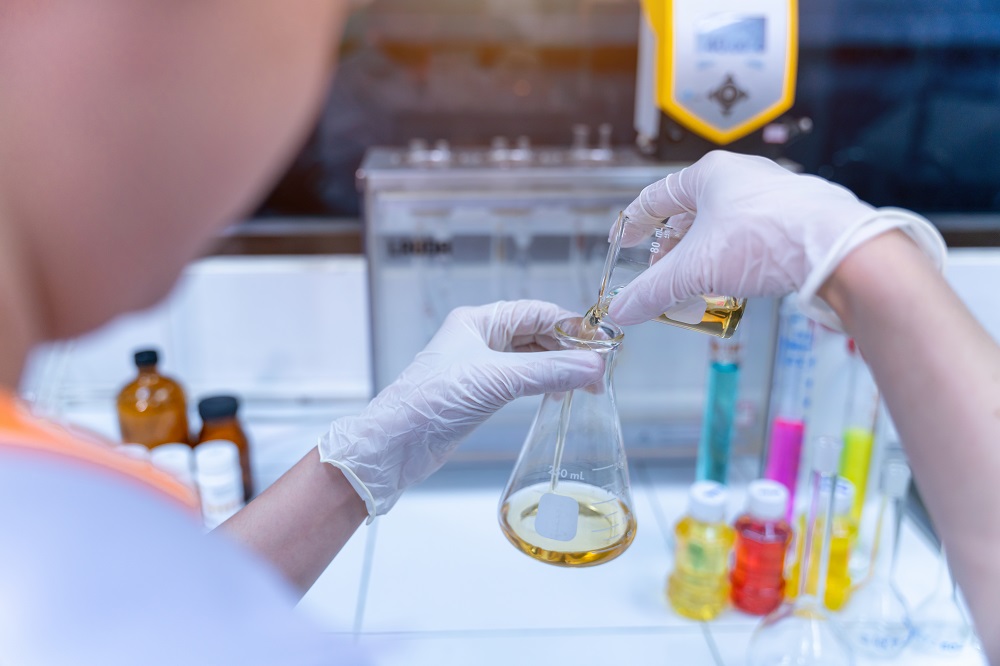 Close up of female hands in sterile gloves pouring yellow liquid into glass tube in oil laboratory experimental concept of oil industry