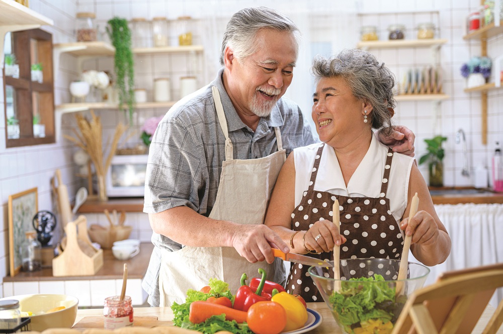 Asian Senior couple wearing apron preparing food in the kitchen. Senior lovers spend time together concept.