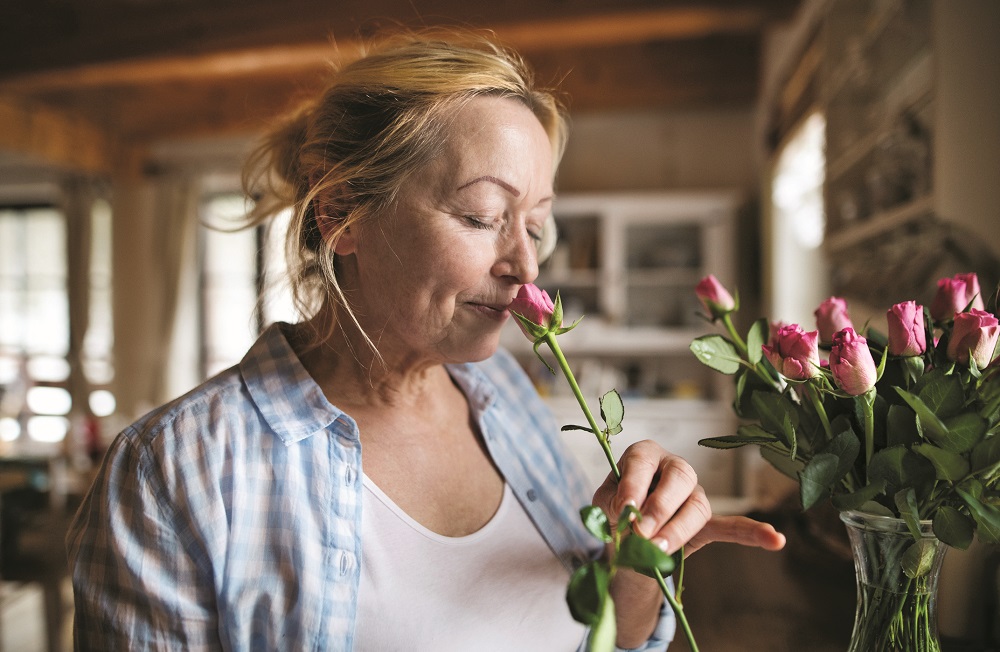 Senior woman in her kitchen smelling fragrance of pink rose