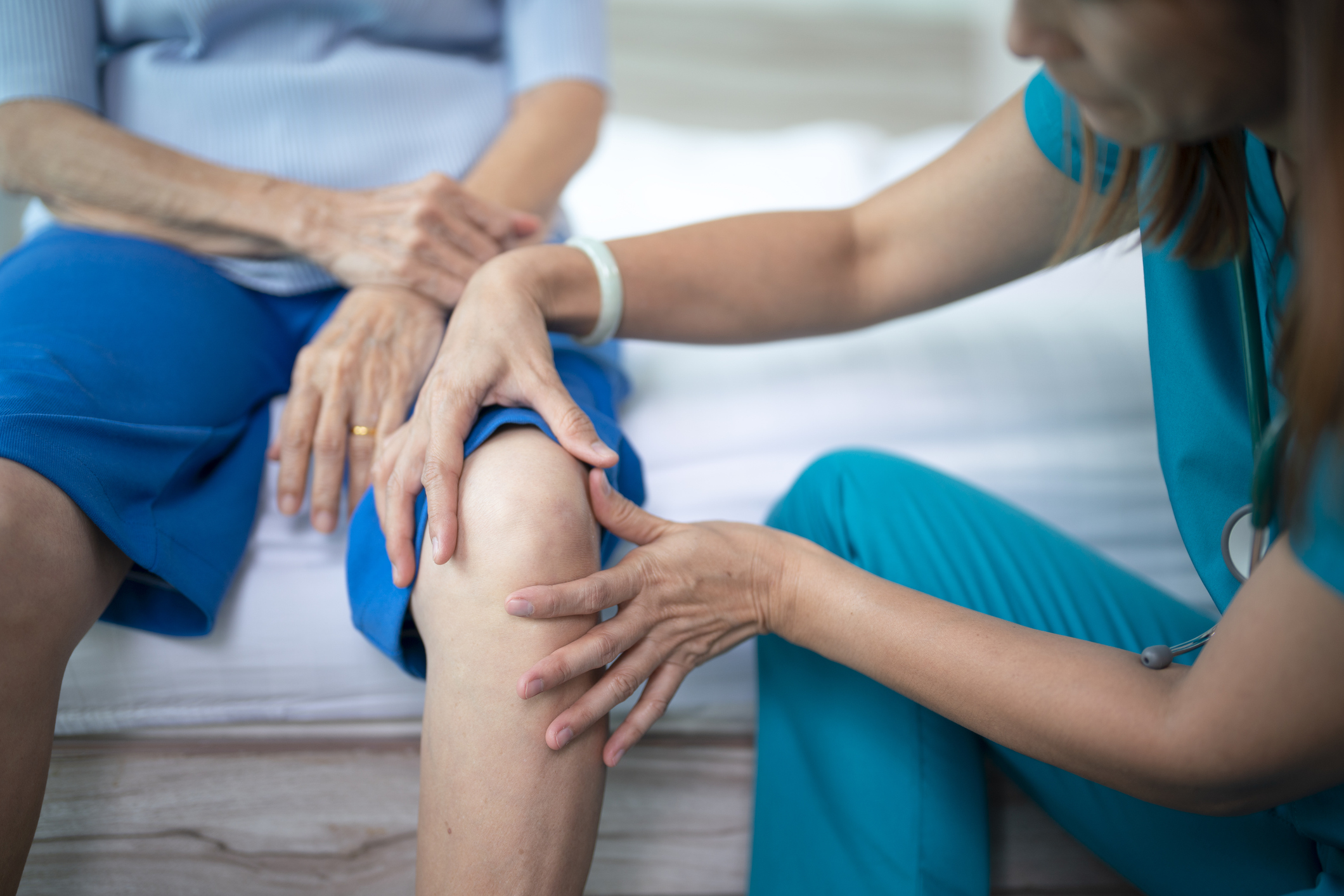 Female nurse home caregiver checking a knee to senior woman