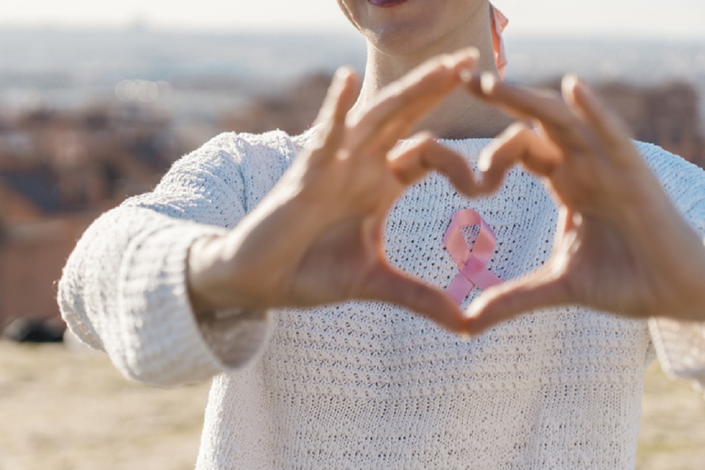Woman making a heart shaped with her hands while using a pink ribbon for support breast cancer cause.