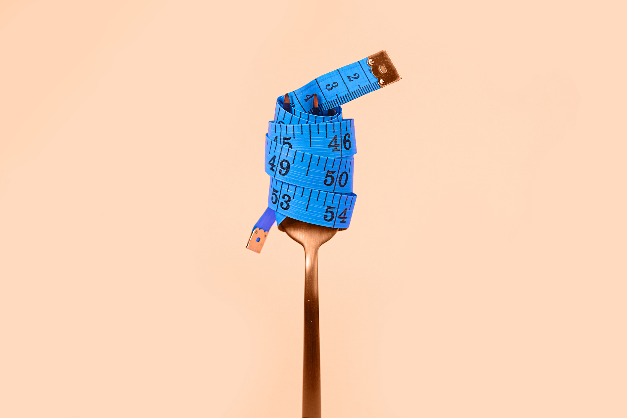 Blue measuring tape and fork on trendy Beige Orange Pink peach color Background.